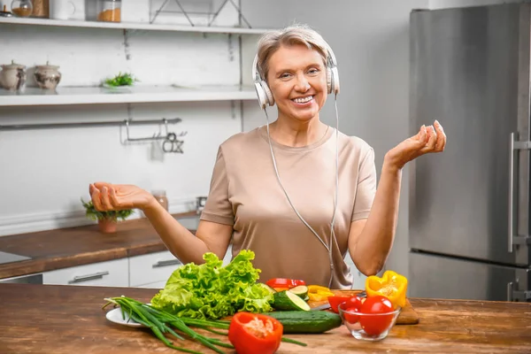 Mature woman listening to music while cooking in kitchen — Stock Photo, Image