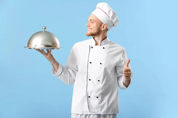 Bonito chef masculino com bandeja e cloche no fundo de cor — Fotografia de Stock