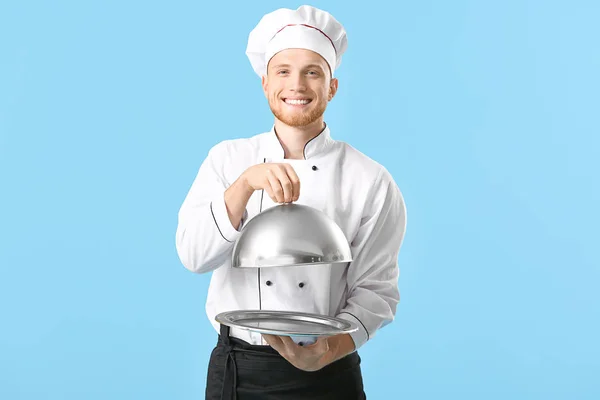 Guapo chef masculino con bandeja y cloche sobre fondo de color —  Fotos de Stock
