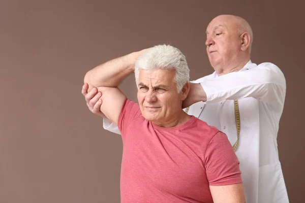 Senior physiotherapist working with mature man on color background — Stock Photo, Image