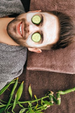 Young man with clay mask on his face in beauty salon