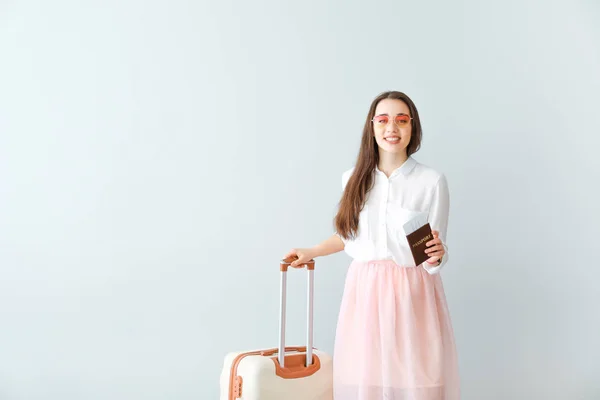 Happy young woman with suitcase, passport and ticket on light background — Stock Photo, Image
