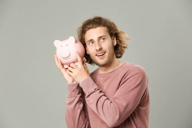 Handsome man with piggy bank on grey background clipart