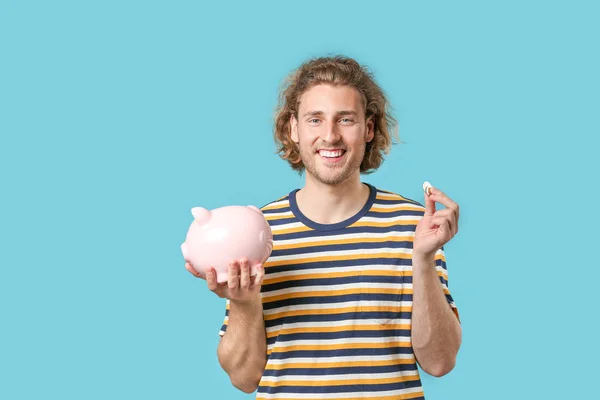 Handsome man with piggy bank on color background — Stock Photo, Image