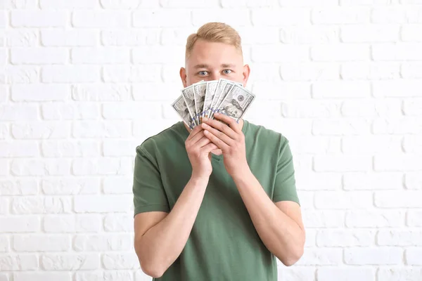 Happy young man with dollar banknotes on white brick background — Stock Photo, Image