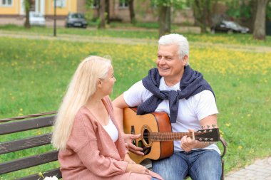 Olgun adam parkta eşi için gitar çalıyor