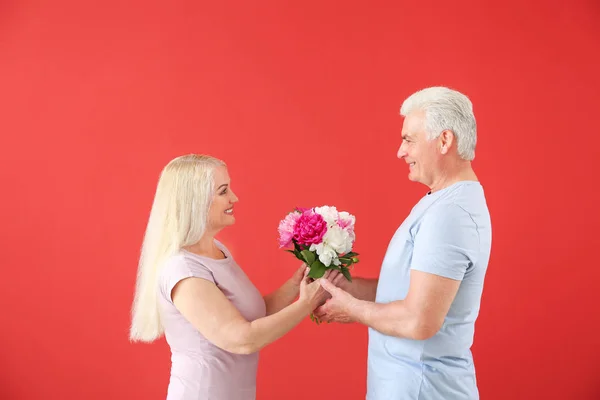 Retrato de feliz pareja madura con flores sobre fondo de color —  Fotos de Stock