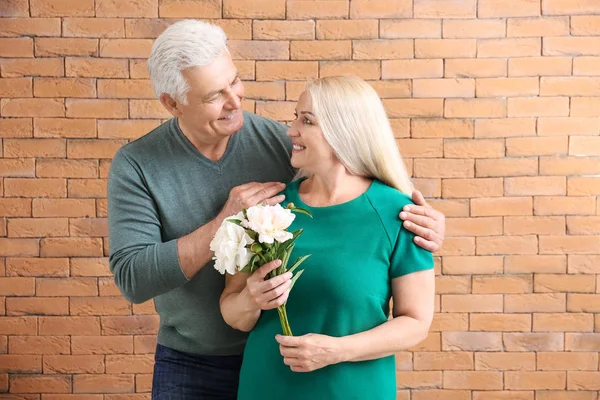 Portrait of happy mature couple with flowers against brick wall — Stock Photo, Image