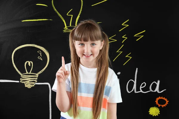 Маленька дівчинка з піднятим індексним пальцем біля намальованих лампочок на темній стіні — стокове фото