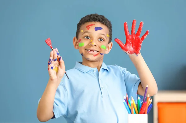 Cute African-American boy with hands and face in paint at home — Stock Photo, Image