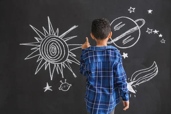 Cute African-American boy drawing space on dark wall