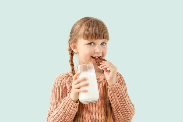 Χαριτωμένο μικρό κορίτσι με ποτήρι γάλα και μπισκότο σε ανοιχτόχρωμο φόντο — Φωτογραφία Αρχείου