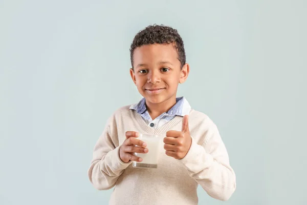 Cute African-American boy with glass of milk showing thumb-up on light background — Stock Photo, Image