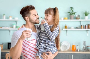 Küçük kızı olan genç bir baba evde lezzetli süt içiyor.