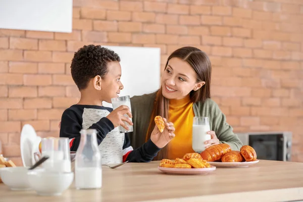 Young mother with adopted son drinking tasty milk in kitchen at home — Stock Photo, Image