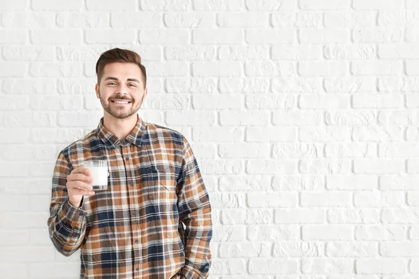 Hombre guapo con vaso de leche sabrosa sobre fondo de ladrillo blanco —  Fotos de Stock