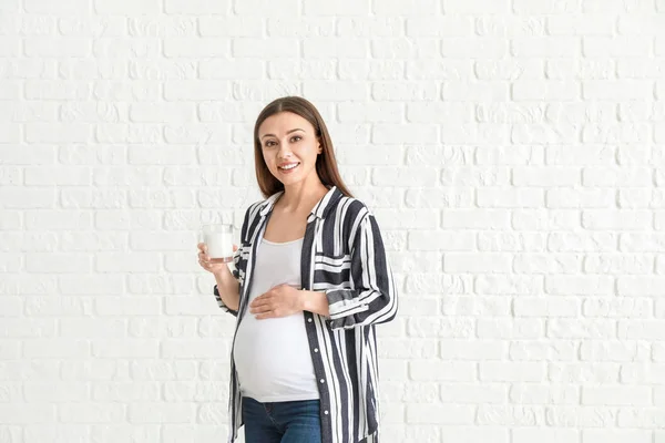 Красивая беременная женщина со стаканом вкусного молока на фоне белого кирпича — стоковое фото
