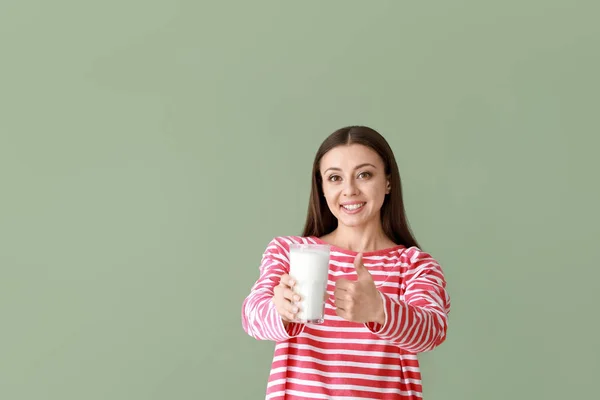 Beautiful woman with glass of tasty milk showing thumb-up gesture on color background — Stock Photo, Image