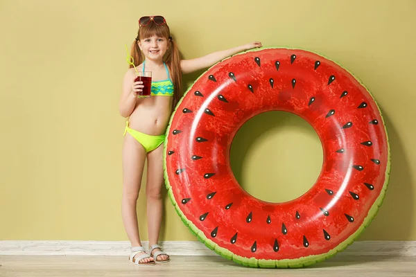 Söt liten flicka med uppblåsbar ring och läsk nära färg väggen — Stockfoto