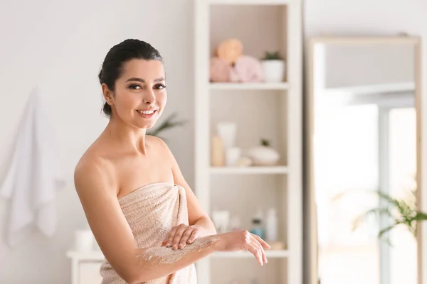 Hermosa mujer joven aplicando exfoliante corporal en casa — Foto de Stock