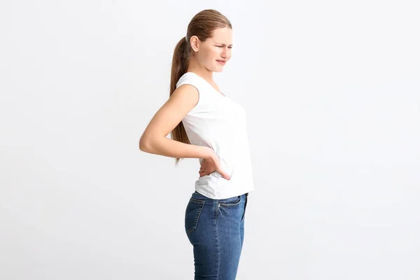 Ung kvinna som lider av ryggsmärta på vit bakgrund — Stockfoto