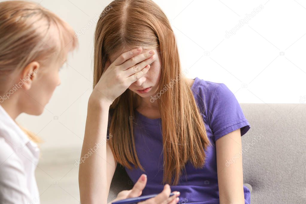 Female psychologist working with sad teenage girl in office