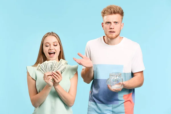 Happy woman with money and confused man with empty jar on color background