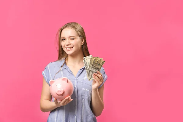 色の背景に貯金箱とお金を持つ幸せな女性 — ストック写真