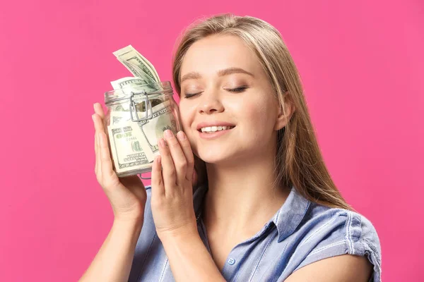 Happy woman with jar full of dollar banknotes on color background — Stock Photo, Image