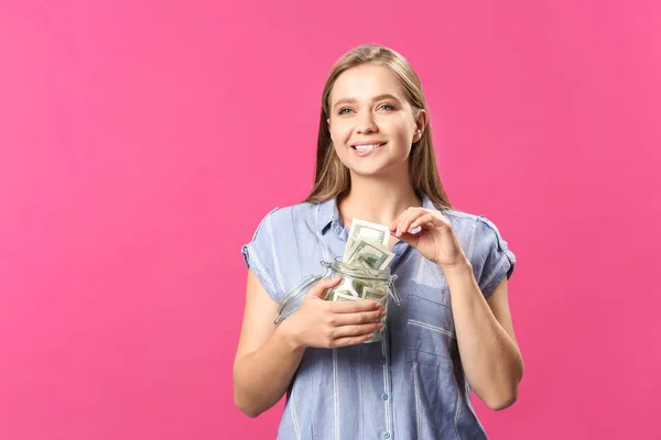 Happy woman with jar full of dollar banknotes on color background — Stock Photo, Image