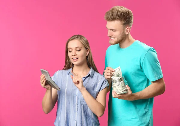 Junges Paar mit Geld im Glas und Taschenrechner auf farbigem Hintergrund — Stockfoto