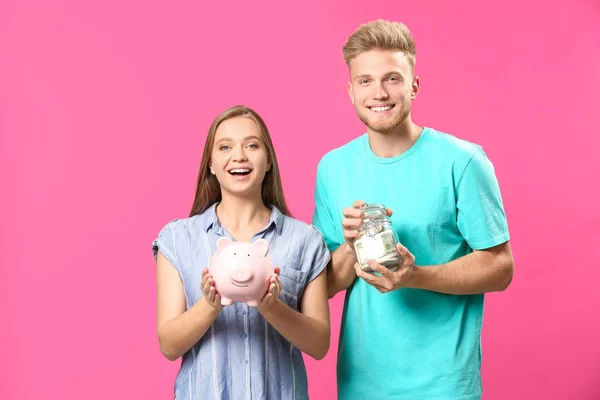 Casal feliz com frasco cheio de notas de dólar e porquinho no fundo de cor — Fotografia de Stock
