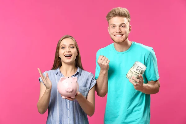 幸福的夫妇与罐子充满了美元钞票和猪银行的颜色背景 — 图库照片