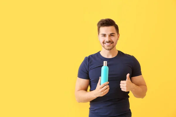 Handsome man with bottle of shampoo showing thumb-up on color background — Stock Photo, Image