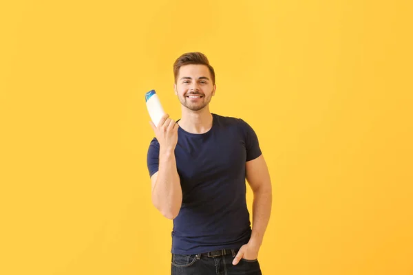 Handsome man with bottle of shampoo on color background — Stock Photo, Image