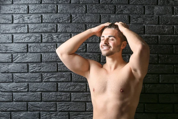 Handsome man washing hair on dark background