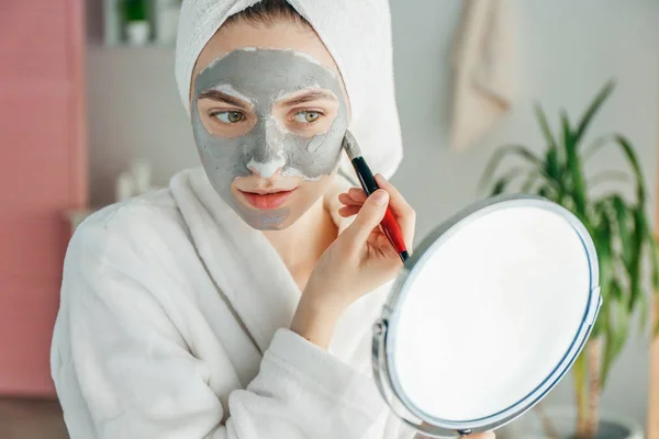 Wanita muda menerapkan masker tanah liat di rumah — Stok Foto