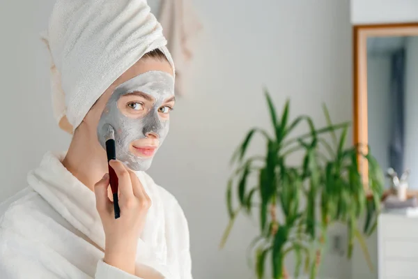 Mujer joven aplicando máscara de arcilla en casa — Foto de Stock