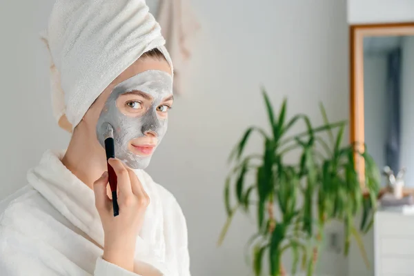 Jonge vrouw het toepassen van klei masker thuis — Stockfoto