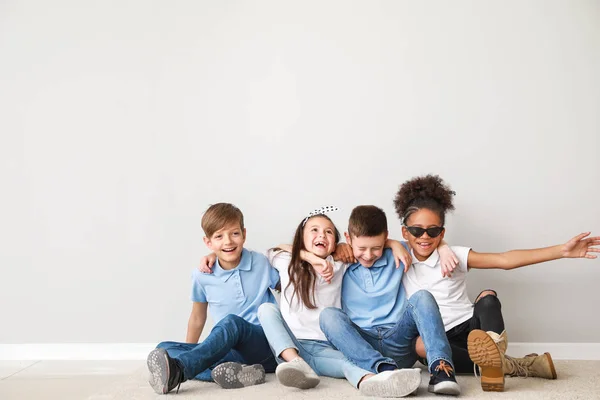 Щасливі діти в джинсах, що сидять біля світлої стіни — стокове фото