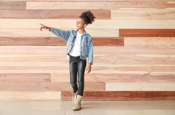Stylish African-American girl in jeans clothes near wooden wall