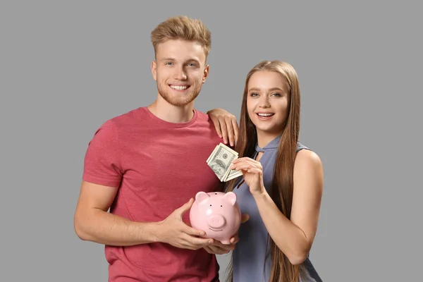 Boldog pár pénzzel és malacka bank szürke háttér — Stock Fotó