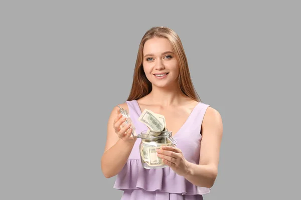 Happy woman with money in jar on grey background — Stock Photo, Image