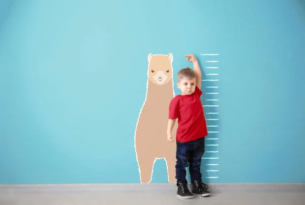 Niño midiendo altura cerca de la pared de color — Foto de Stock