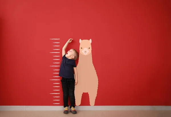 Surprised little boy measuring height near color wall — Stock Photo, Image