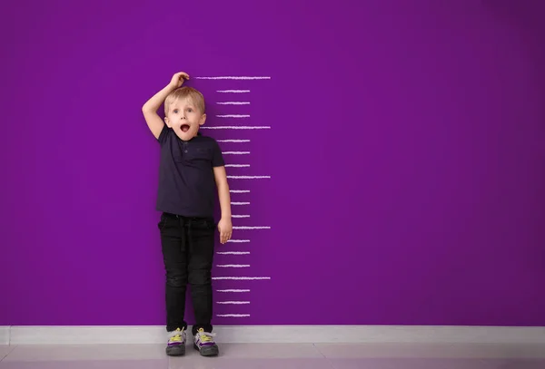 Surprised little boy measuring height near color wall — Stock Photo, Image