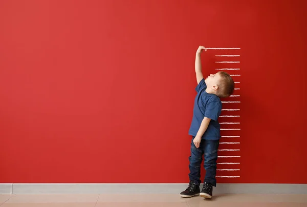 Маленький мальчик измеряет высоту рядом с цветной стеной — стоковое фото
