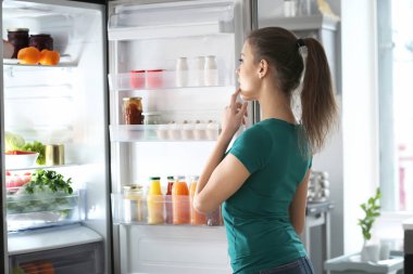 Woman standing near open fridge at home clipart