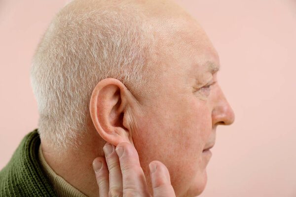 Старший мужчина с проблемами со слухом на фоне цвета
