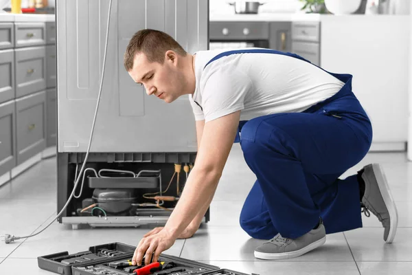 Male technician repairing refrigerator in kitchen